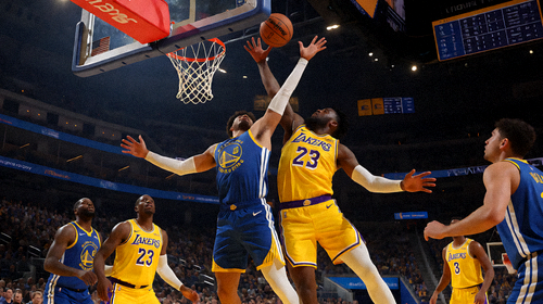NBA洛杉矶湖人对阵金州勇士的比赛现场，在明亮的球馆灯光下，球员们在篮筐附近激烈争夺
